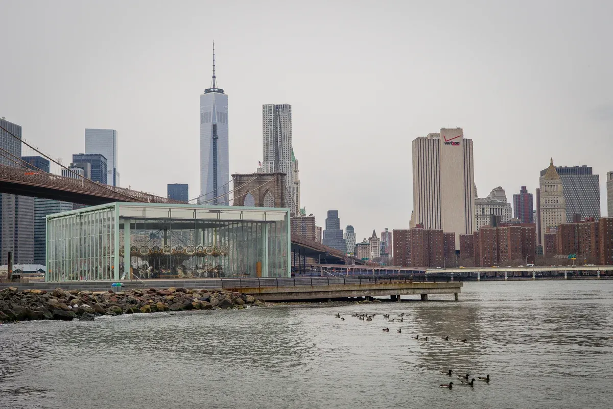 The glass pavilion of Jane's Carousel in front of the Brooklyn Bridge and Lower Manhattan, on a New York architecture tour